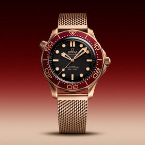 Omega Seamaster Diver 300M Bronze Gold men's automatic watch, 42mm bronze gold case, black dial, burgundy bezel, mesh bracelet – front view on burgundy background