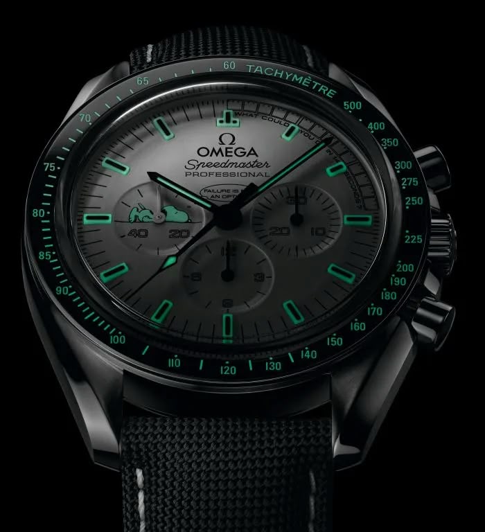 Omega Speedmaster Snoopy Award men's chronograph watch, 42mm stainless steel case, white dial with black subdials, black fabric strap – luminous dial dark view