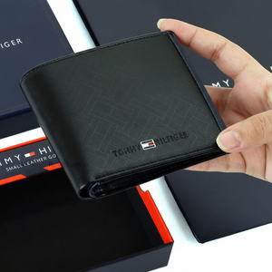 Hand holding a Tommy Hilfiger black leather wallet featuring a subtle textured pattern and the iconic small enamel flag logo