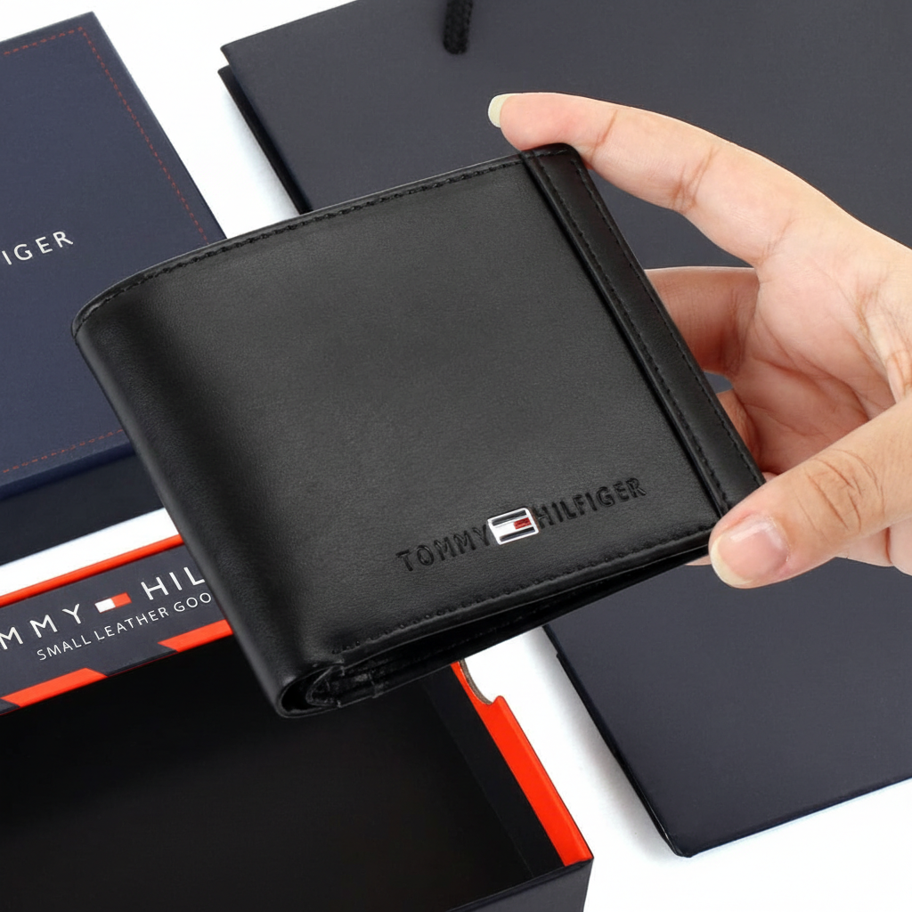 Handheld view of a Tommy Hilfiger men's black leather wallet, showing its compact size and the refined metal flag emblem