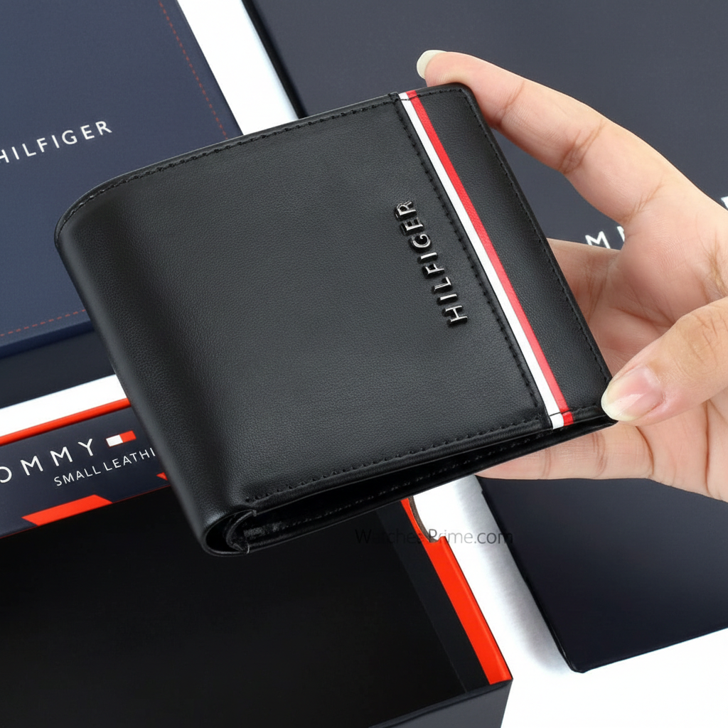 Hand holding a Tommy Hilfiger black smooth leather wallet featuring a vertical raised metal logo and horizontal signature stripe
