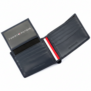 Hand holding a Tommy Hilfiger black leather wallet featuring a vertical tricolor signature stripe and a raised silver metal Hilfiger logo
