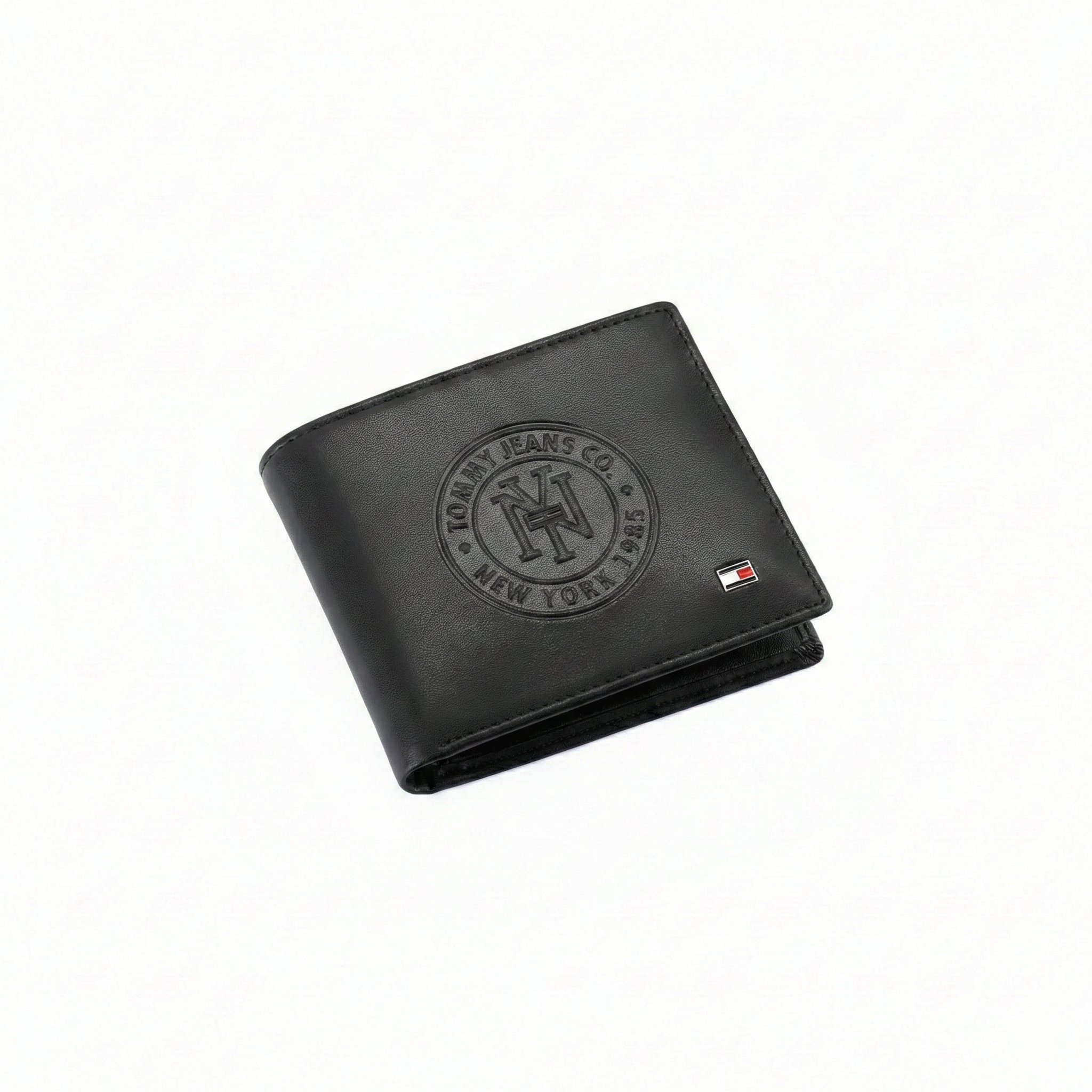 Angled view of Tommy Hilfiger black men's wallet highlighting large embossed Tommy Jeans Co New York 1985 heritage logo and small metal flag