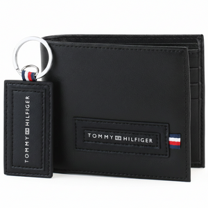 Close-up display of a Tommy Hilfiger men's black leather wallet leaning against a matching keychain, highlighting the stitched logo patches on both items