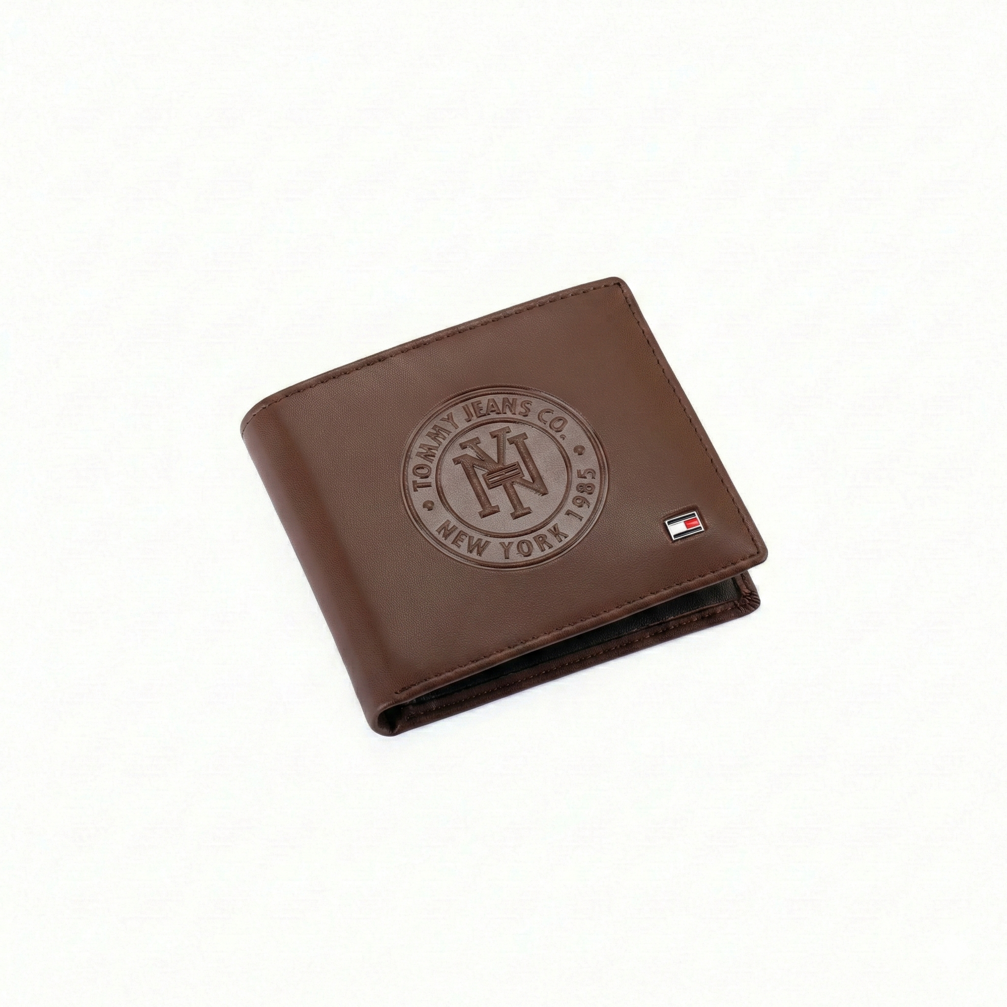 Angled view of Tommy Hilfiger brown men's wallet featuring large Tommy Jeans Co 1985 embossed circle logo and stitching details