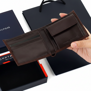 An open display of the Tommy Hilfiger men's brown leather wallet alongside its branded gift box and shopping bag, showcasing a complete luxury presentation