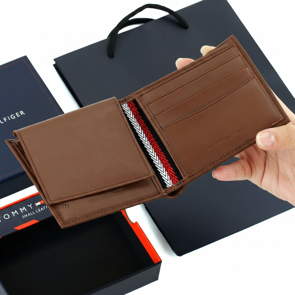 Handheld display of an open Tommy Hilfiger brown leather wallet, showcasing the internal compartments and embossed brand name