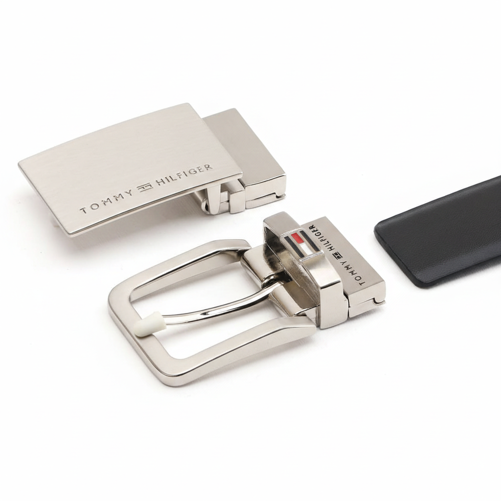 Close-up view of two premium Tommy Hilfiger metal buckles included in the gift set: a modern plaque buckle with engraved logo and a classic pin buckle with the signature flag logo