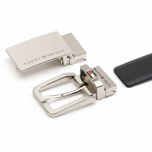 Close-up view of two premium Tommy Hilfiger metal buckles included in the gift set: a modern plaque buckle with engraved logo and a classic pin buckle with the signature flag logo