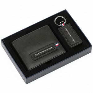 Top-down view of a Tommy Hilfiger men's black leather wallet and matching keychain securely presented inside their original navy blue open gift box