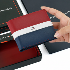 Hand holding a Tommy Hilfiger men's leather wallet featuring a bold red, white, and navy blue horizontal stripe design, displayed above its open gift box