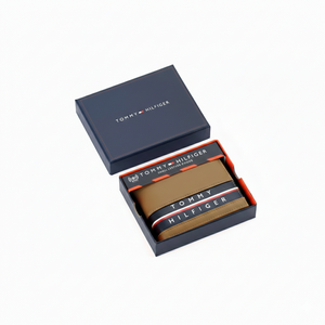 Authentic Tommy Hilfiger men's tan and navy blue genuine leather bifold wallet featuring the iconic brand name stripe, presented in a premium navy gift box
