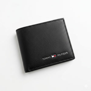 Professional angled studio photograph of the sleek Tommy Hilfiger mirror original smooth black leather bifold wallet showcasing the enamel flag and silver branding