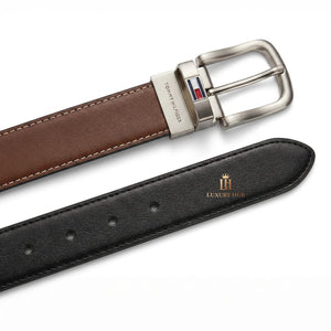Close-up product photography of the Tommy Hilfiger reversible leather belt showcasing the polished silver rotatable buckle engraved with brand text alongside black and brown leather sides