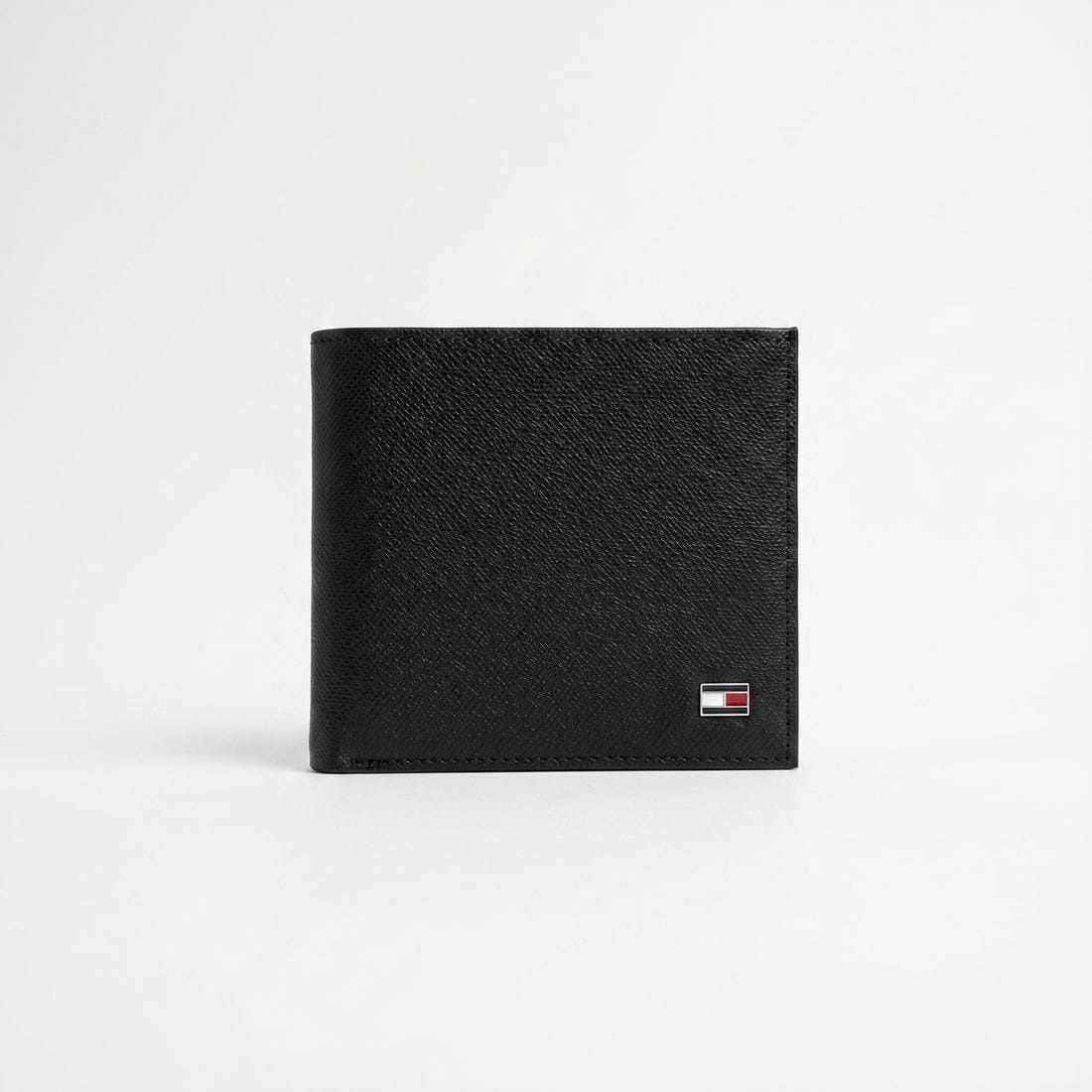 Live front view smartphone photograph of the Tommy Hilfiger smooth black leather wallet highlighting the tiny iconic enamel flag metal logo corner accent