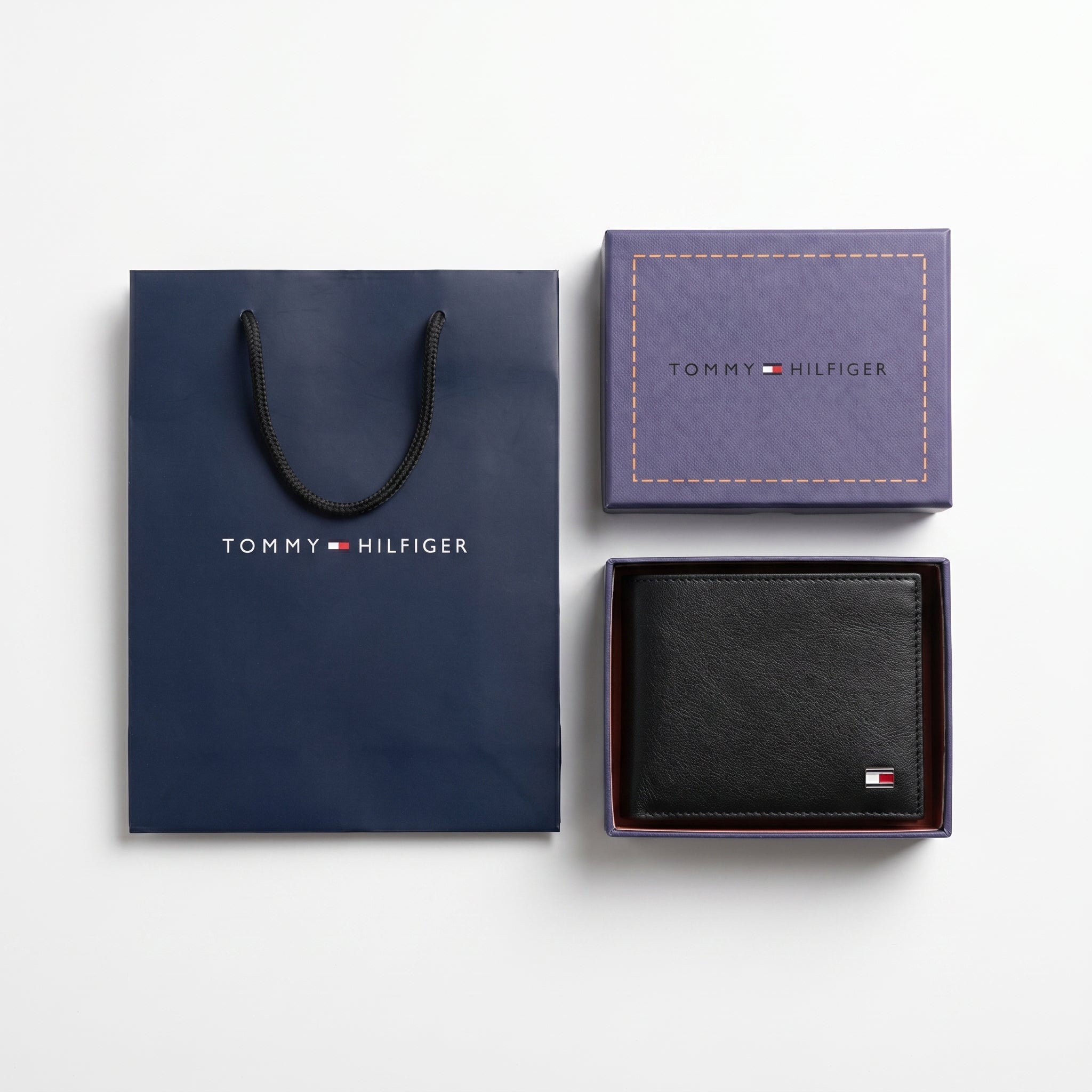 Full premium packaging presentation of the Tommy Hilfiger mirror original textured black leather bifold wallet alongside its navy gift box and matching shopping bag