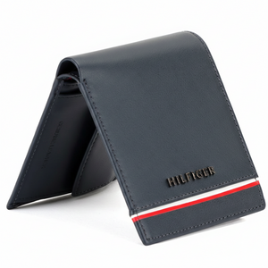 Side view of a standing Tommy Hilfiger navy genuine leather bifold wallet showcasing its sleek profile and the signature red, white, and blue vertical stripe