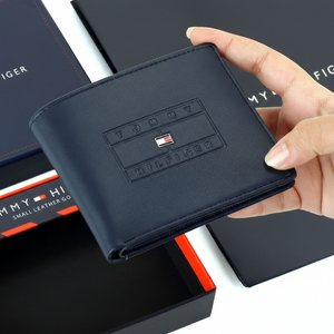 Hand holding a black wallet with a brand logo, placed on branded packaging.
