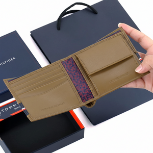 Handheld view of the open Tommy Hilfiger tan leather wallet alongside its branded gift box and luxury shopping bag