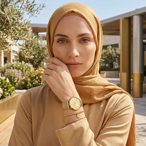 Elegant woman wearing Guess U1155L3 women's quartz battery watch with gold case and luxury striped mesh bracelet