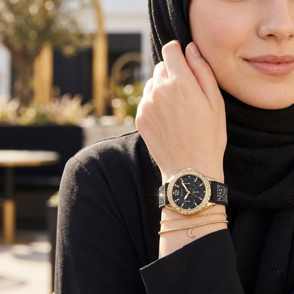 Elegant woman wearing Guess Swirl W1096L3 women's quartz battery watch with gold case and luxury crystal black rubber strap