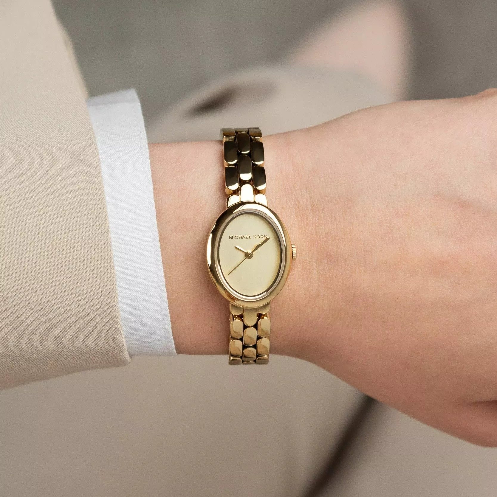 Gold watch on a wrist with a neutral background